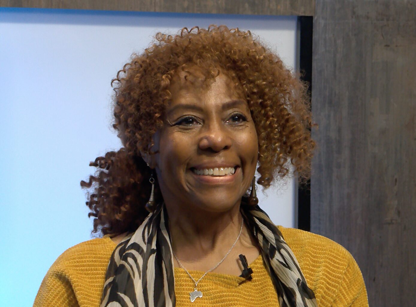 Marvinetta wearing a bright yellow shirt and smiling brightly, sitting in the studio at PMN.